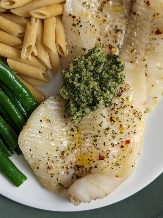 Our baked flounder topped with homemade pesto and served on a plate pasta and green beans.