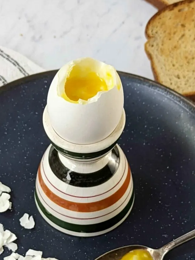 A perfectly cooked soft boiled egg cracked open with toast in the background.