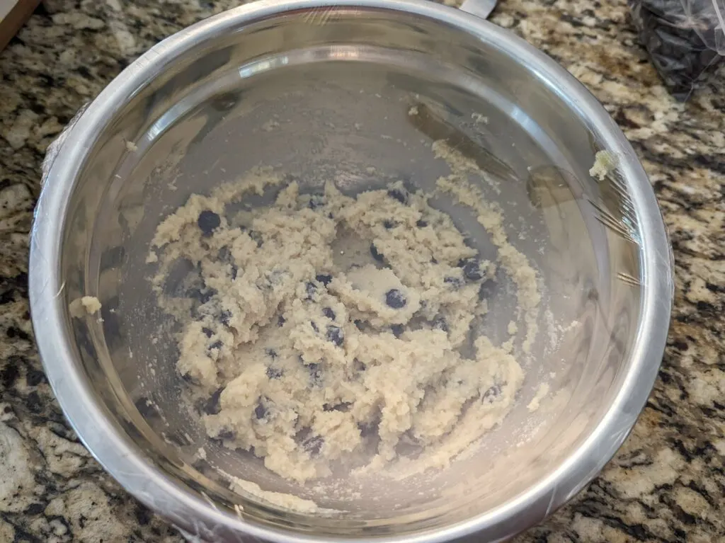 A mixing bowl of cookie dough covered with plastic wrap.
