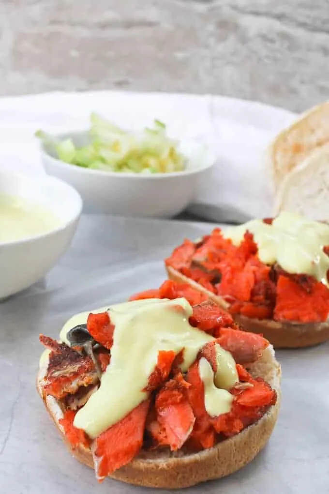 Two slow-roasted salmon sandwiches being drizzled with mustard sauce.