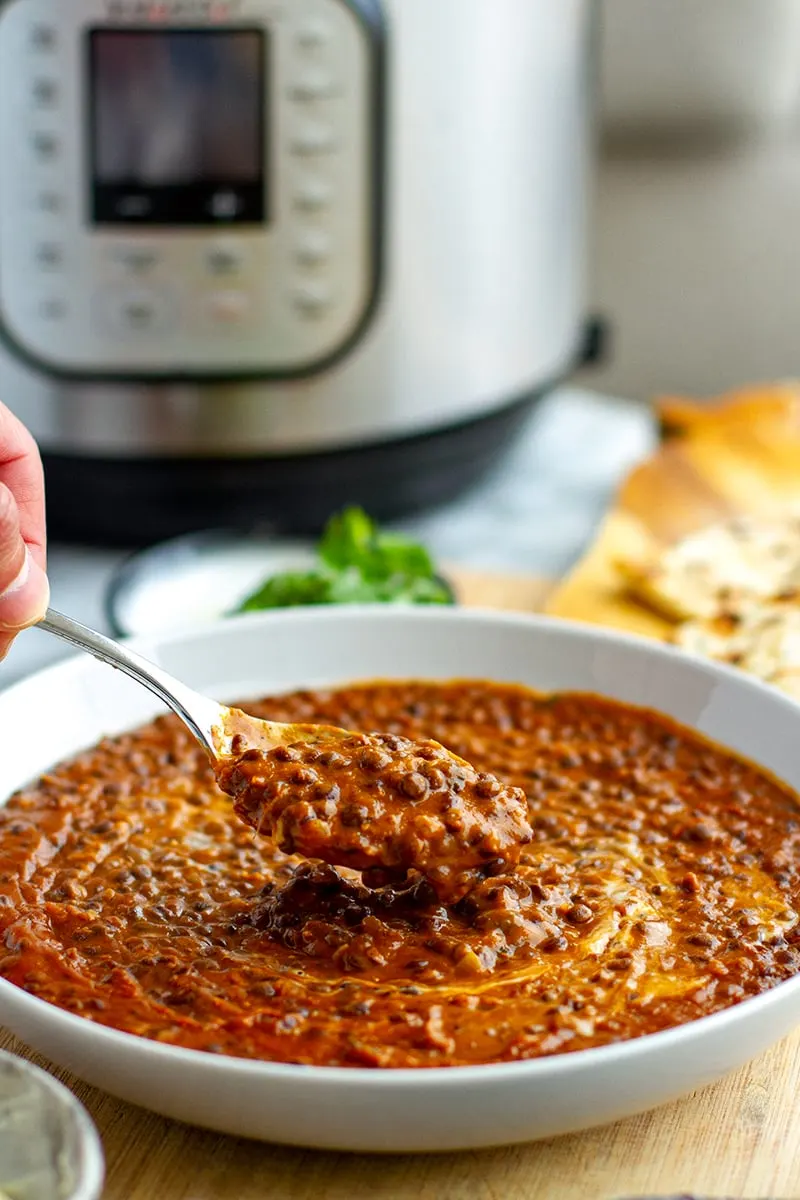 Instant Pot black dal with a spoon scooping it out and an Instant Pot and naan in the background.