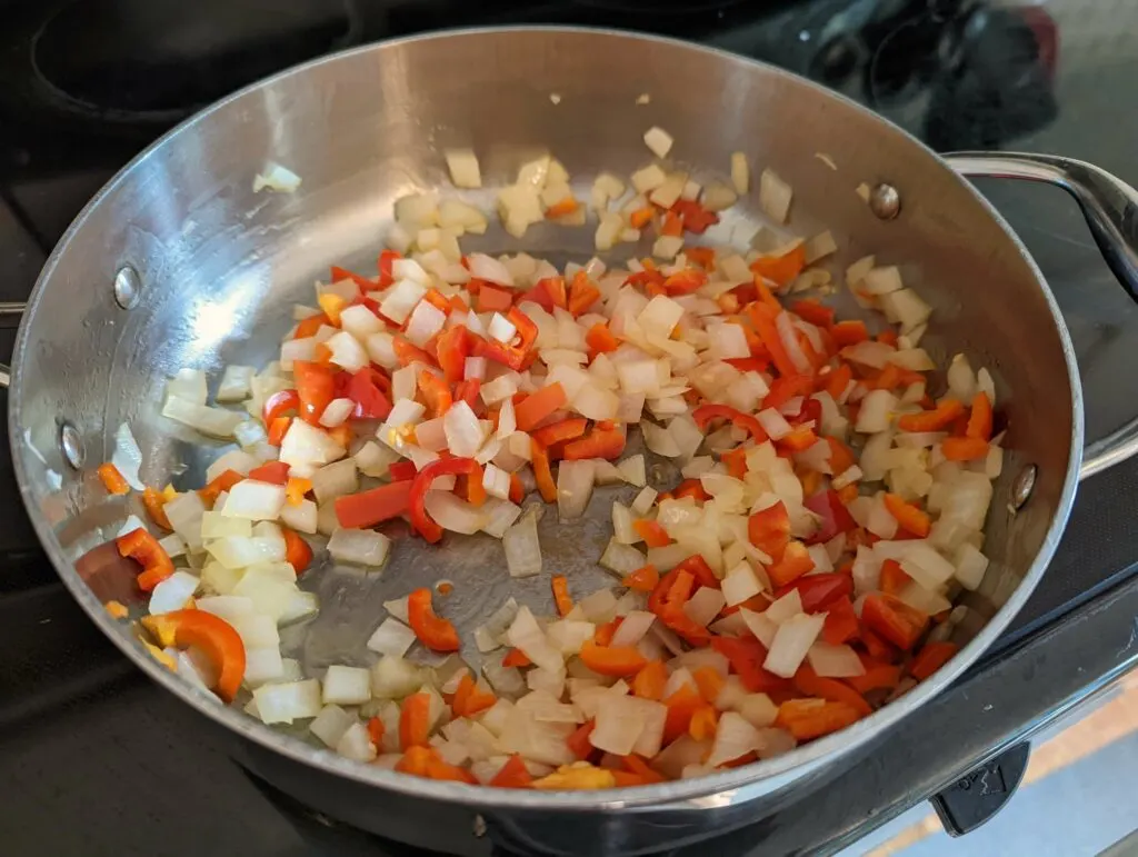 Onions, peppers, and garlic cooking in a pan.