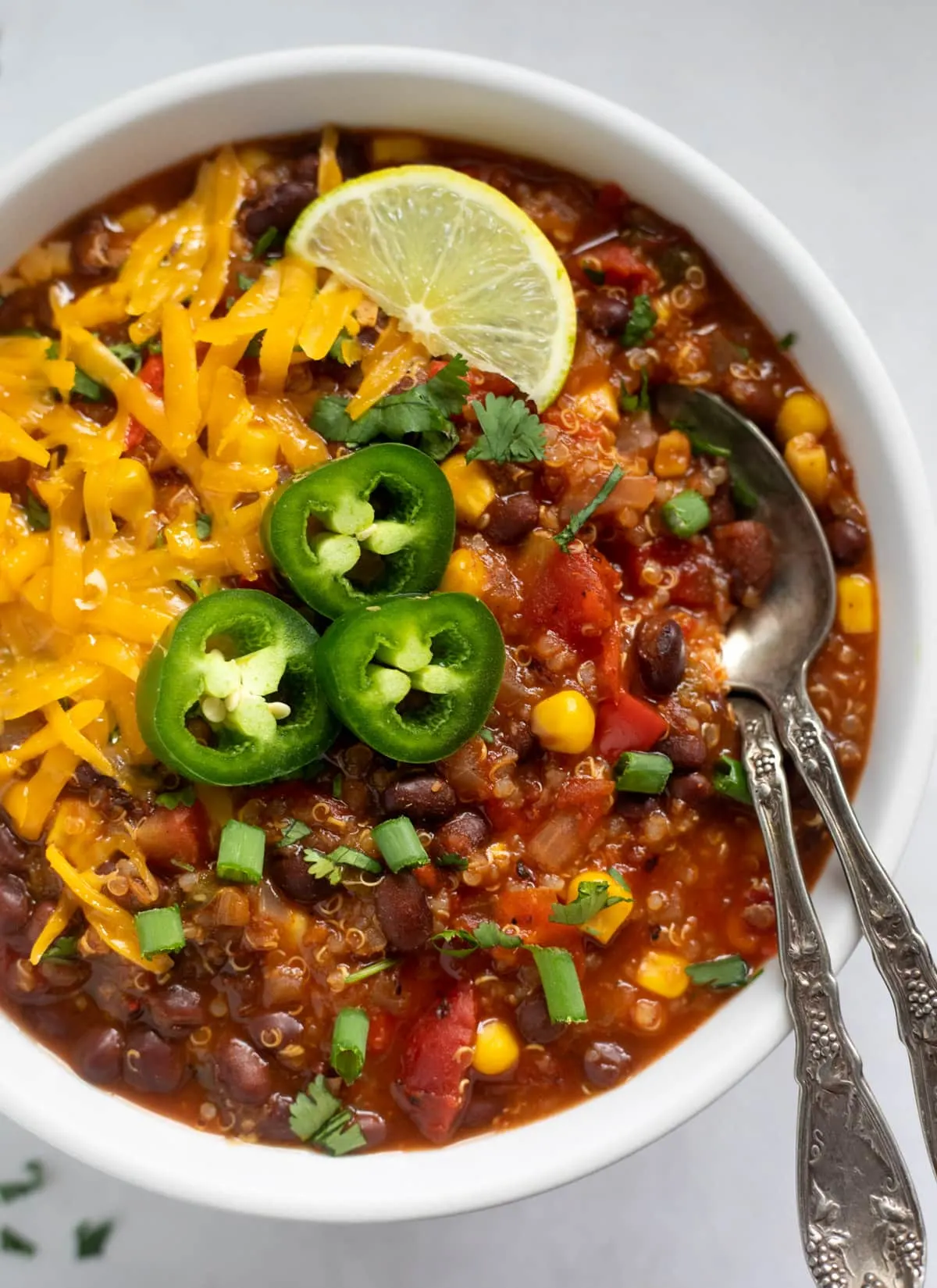 An overhead shot of vegetarian chili garnished with jalapeños, cheddar cheese, and a lime wedge.