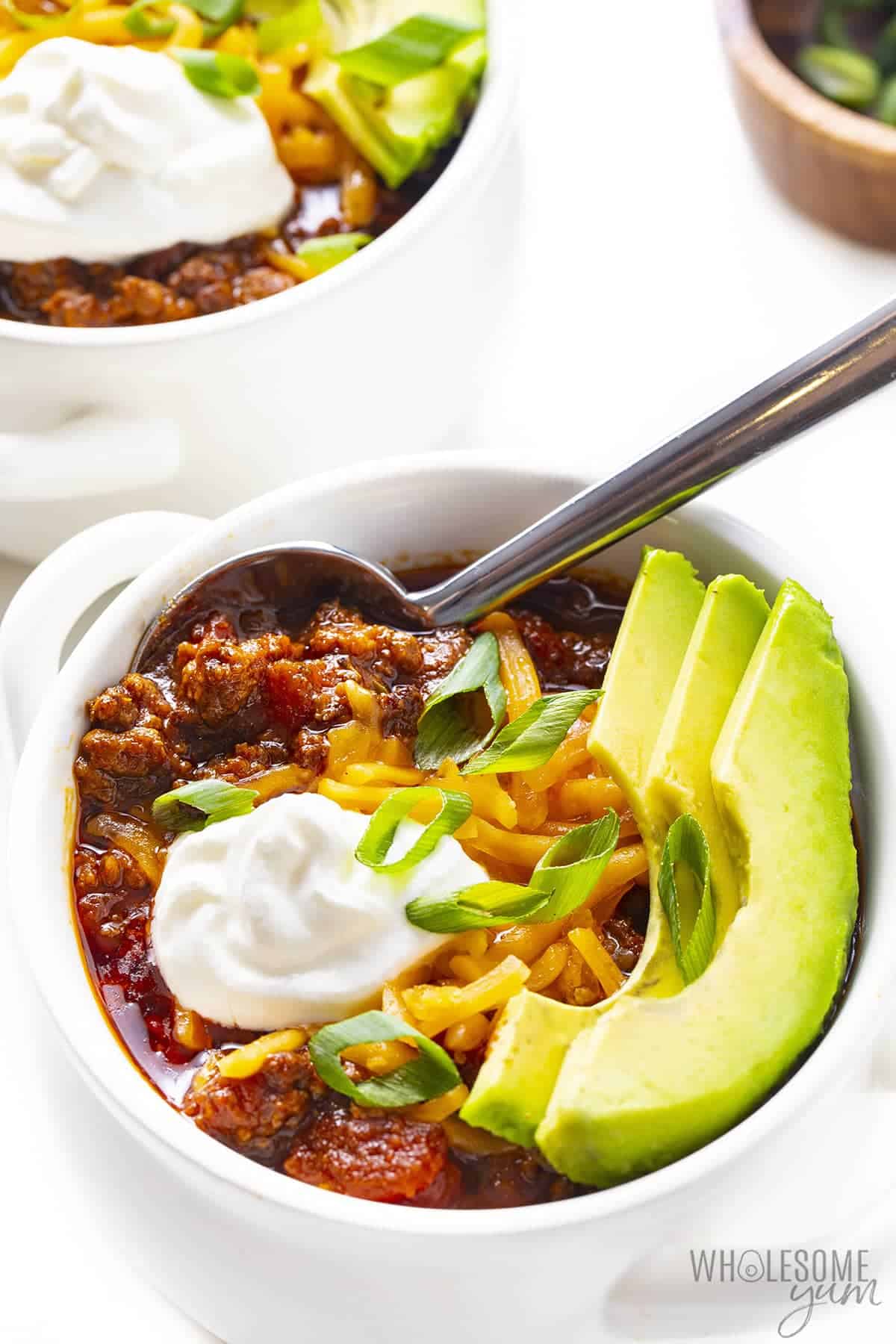Low Carb keto chili in bowl with cheese, sour cream, avocado, and green onion.