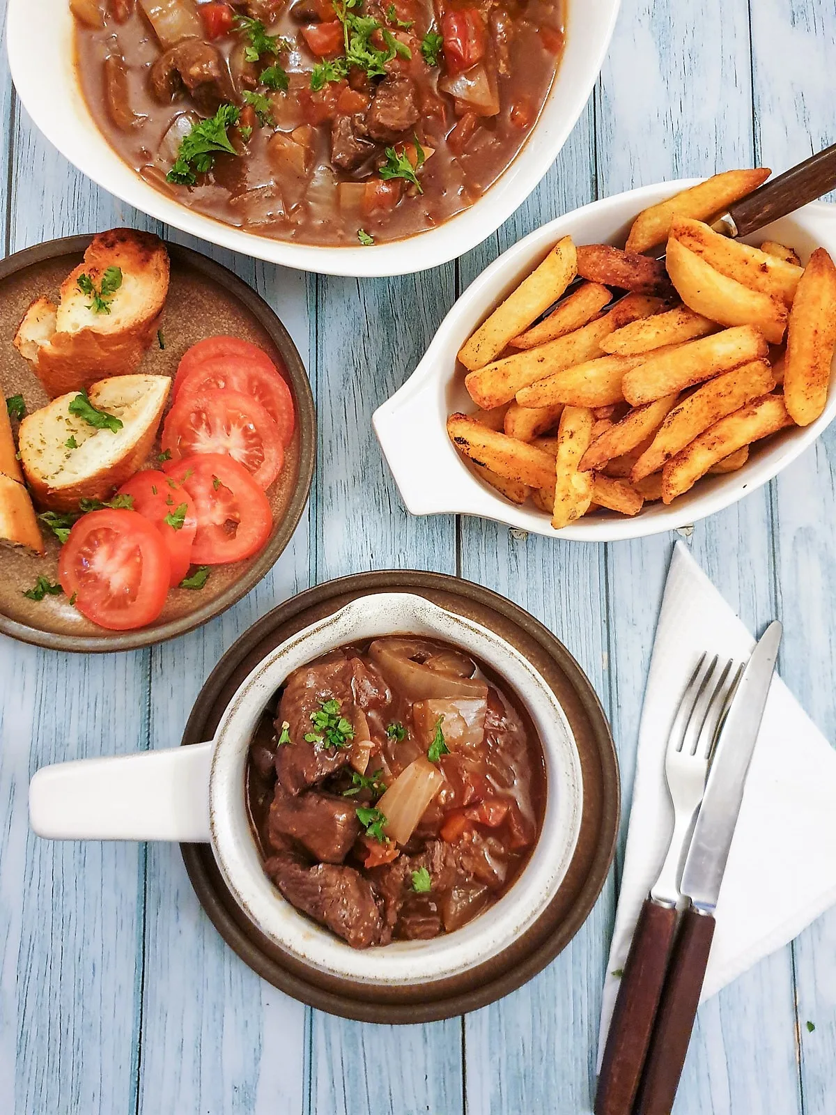 A bowl of beef trinchado served with fries, beans, and a plate of fresh tomatoes and lemons.