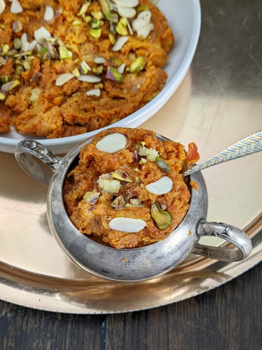 Carrot halwa in a serving dish and garnished with toasted pistachio and almond.