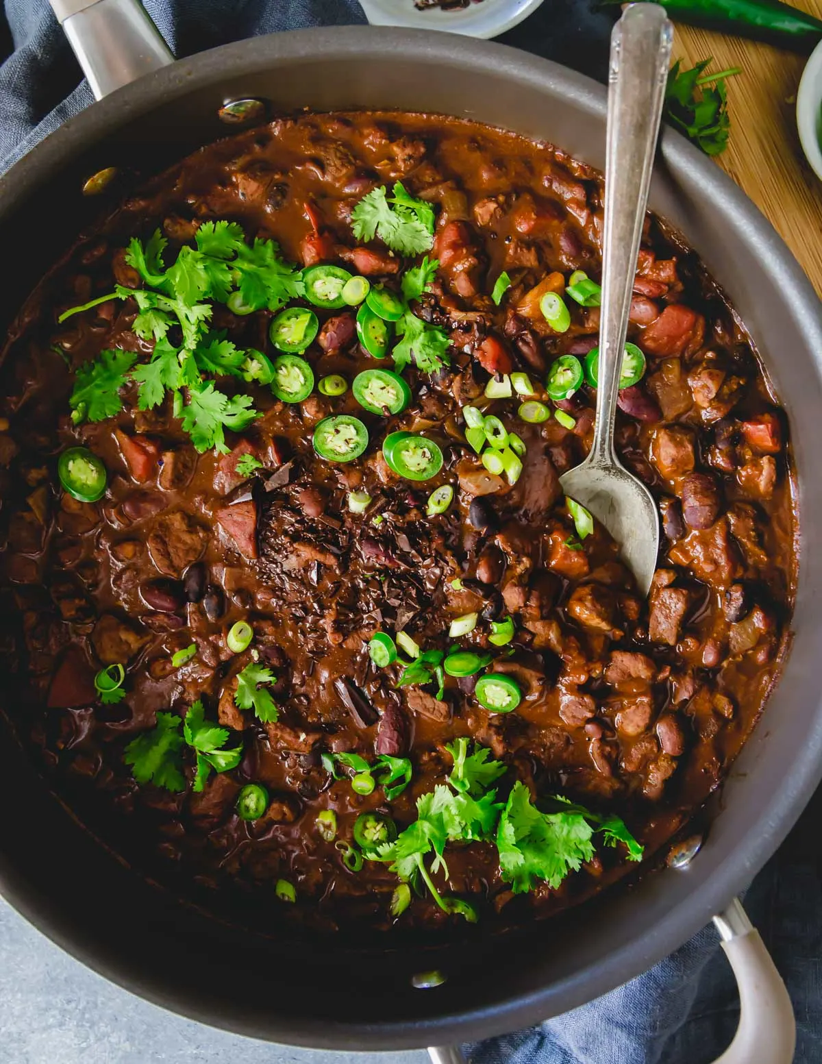 A Dutch oven of chocolate lamb chili topped with chilies and cilantro.