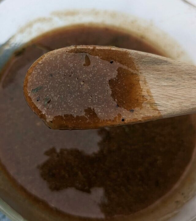 A spoonful of gravy over a saute pan full of gravy.