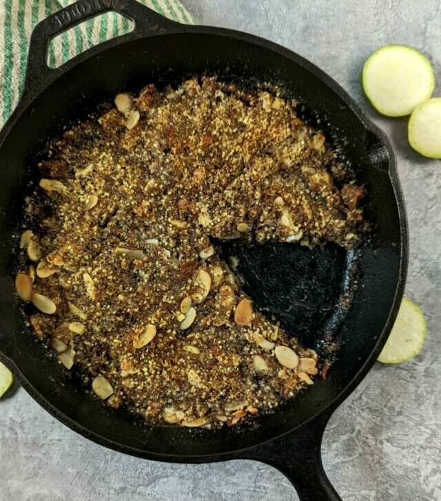 A pan of keto apple crisp with a slice missing and fresh zucchini in the background.