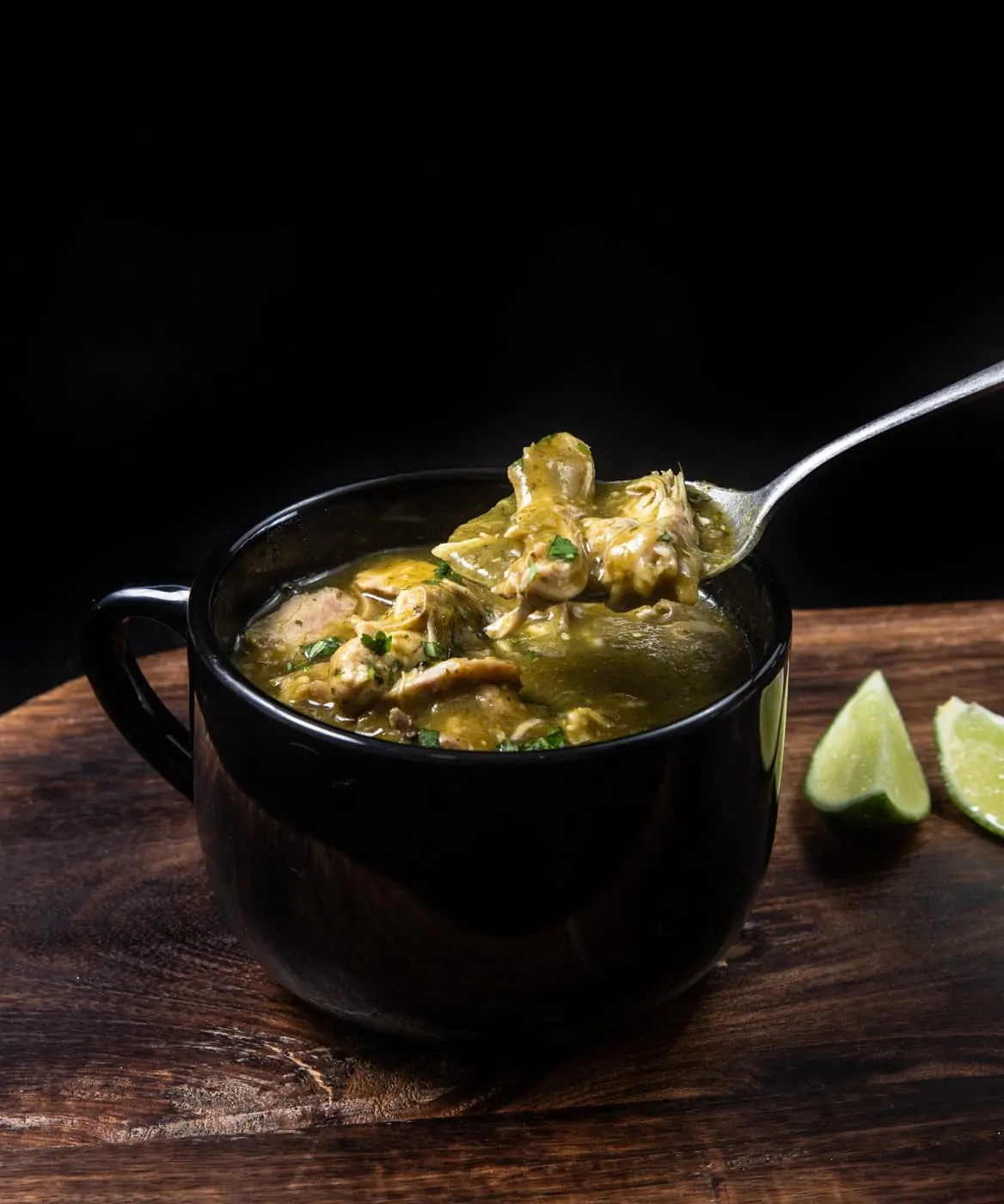A side view of instant pot green chili served with lime wedges.