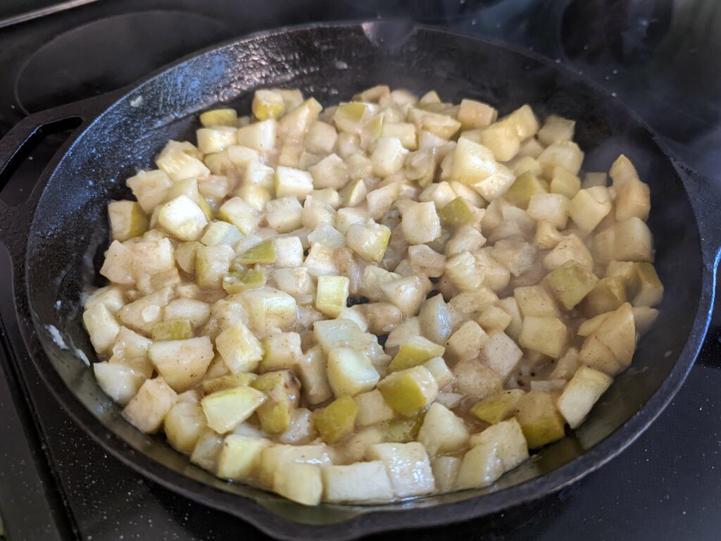 Sugar and cinnamon mixture added to the apples cooking in the pan. 