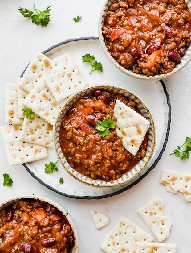 A overhead shot of three bowls of sweet and spicy chili served with saltine crackers and garnished with parsley.