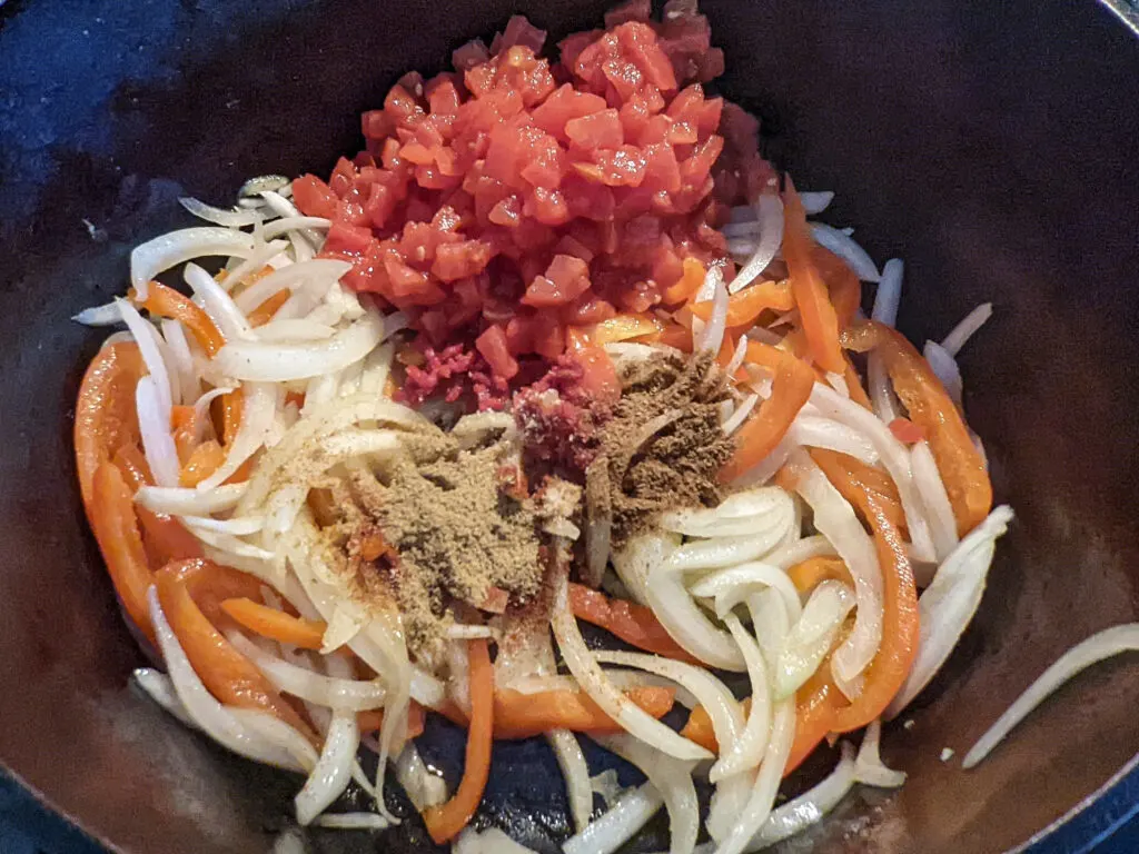 Onions and peppers sautéing in a pot and adding spices, tomatoes, and tomato paste.