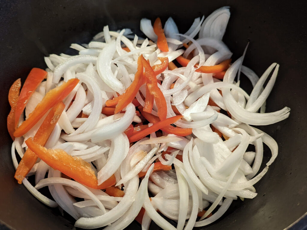 Onions and peppers sautéing in a pot.