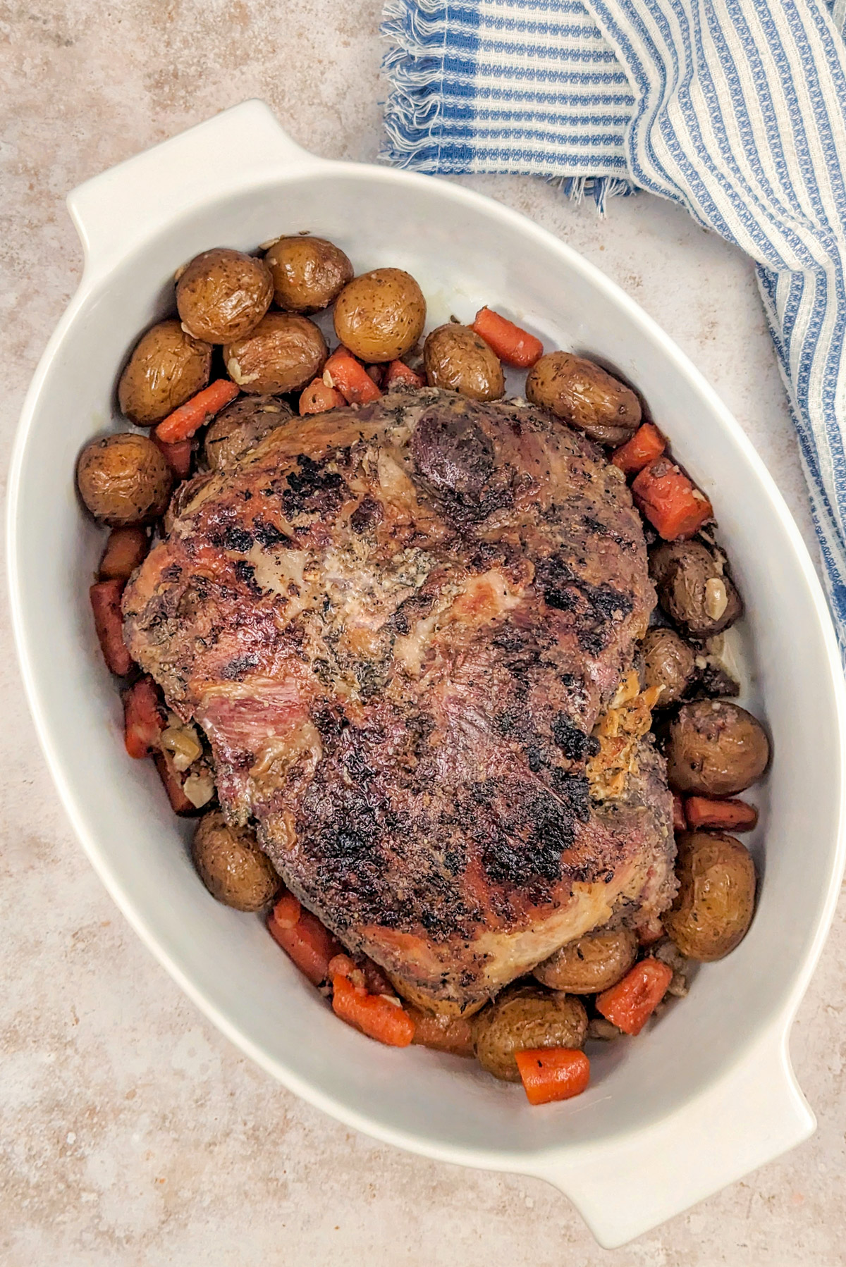 Boneless leg of lamb in a serving bowl with vegetables.