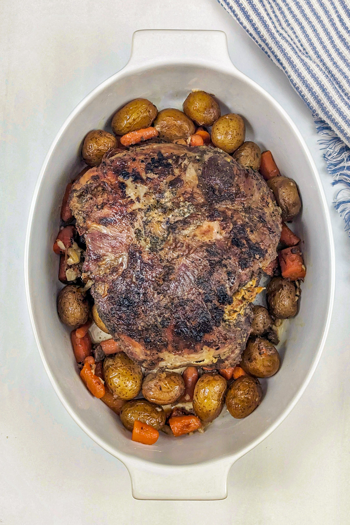 Boneless leg of lamb in a serving bowl with vegetables.