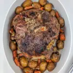 A lamb roast and vegetables in a serving bowl.