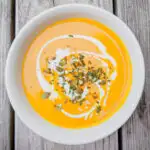 Two bowls of butternut soup topped with pumpkin seeds.