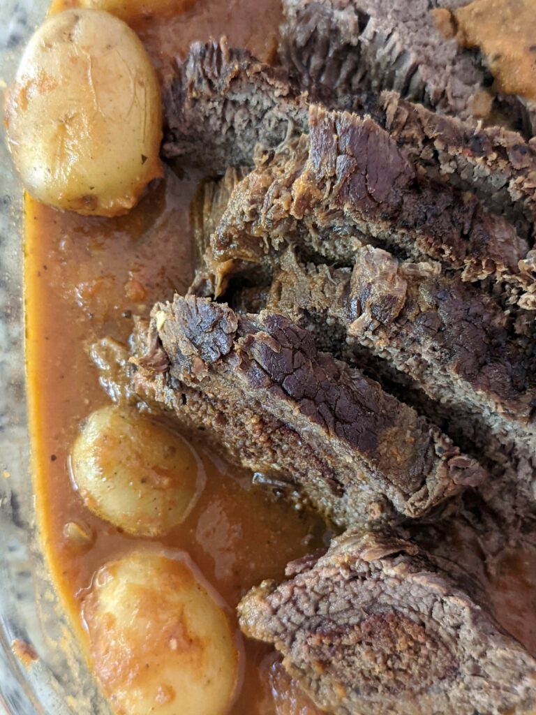 Roast sliced in a serving tray with petite potatoes and gravy.