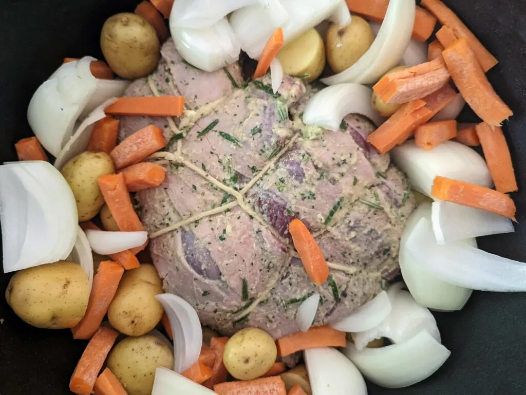 Boneless leg of lamb nestled with onion, potato, and carrots.