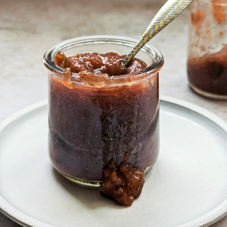 Two jars with fig jam in it and some of the jam spilling out.