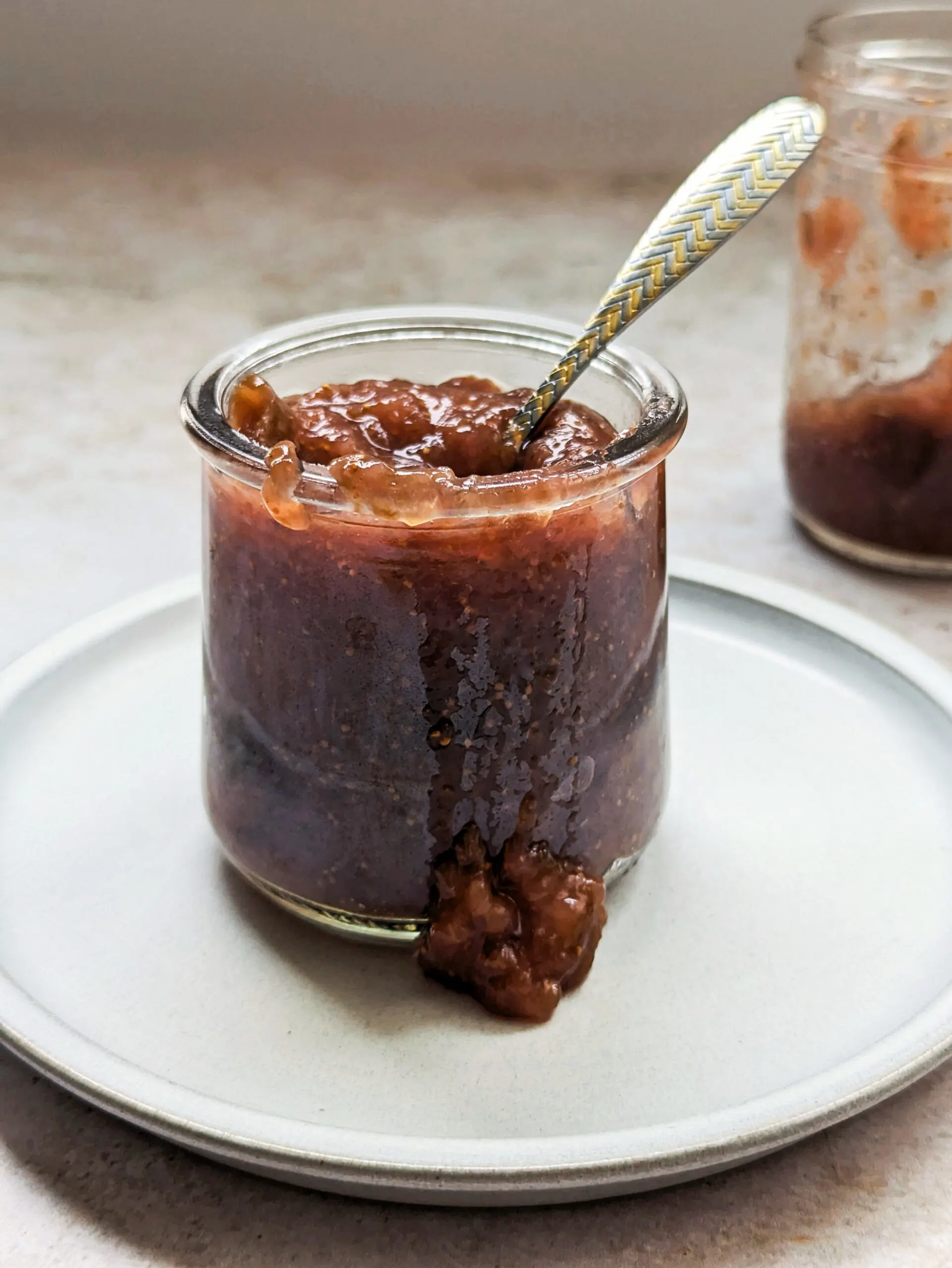 Two jars with fig jam in it and some of the jam spilling out.