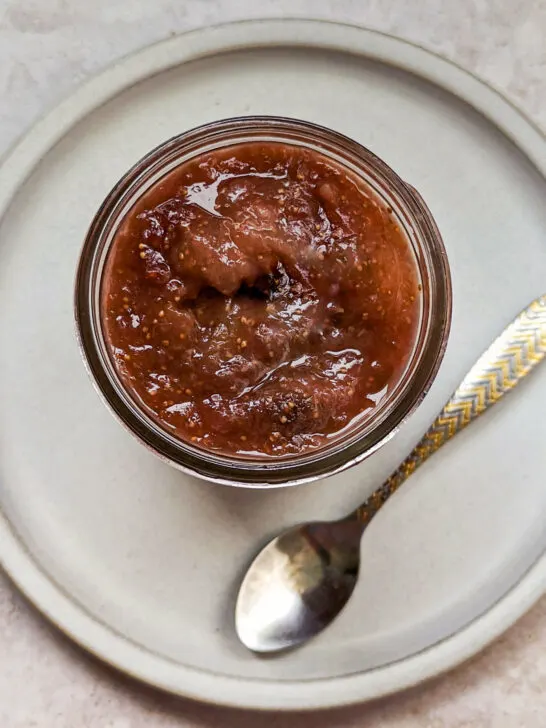 An overhead view of our fig jam recipe in a jar on a plate with a spoon.