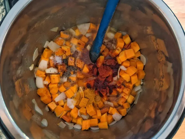 Spices added to the butternut squash, carrot, onion, and garlic cooking in an Instant Pot.