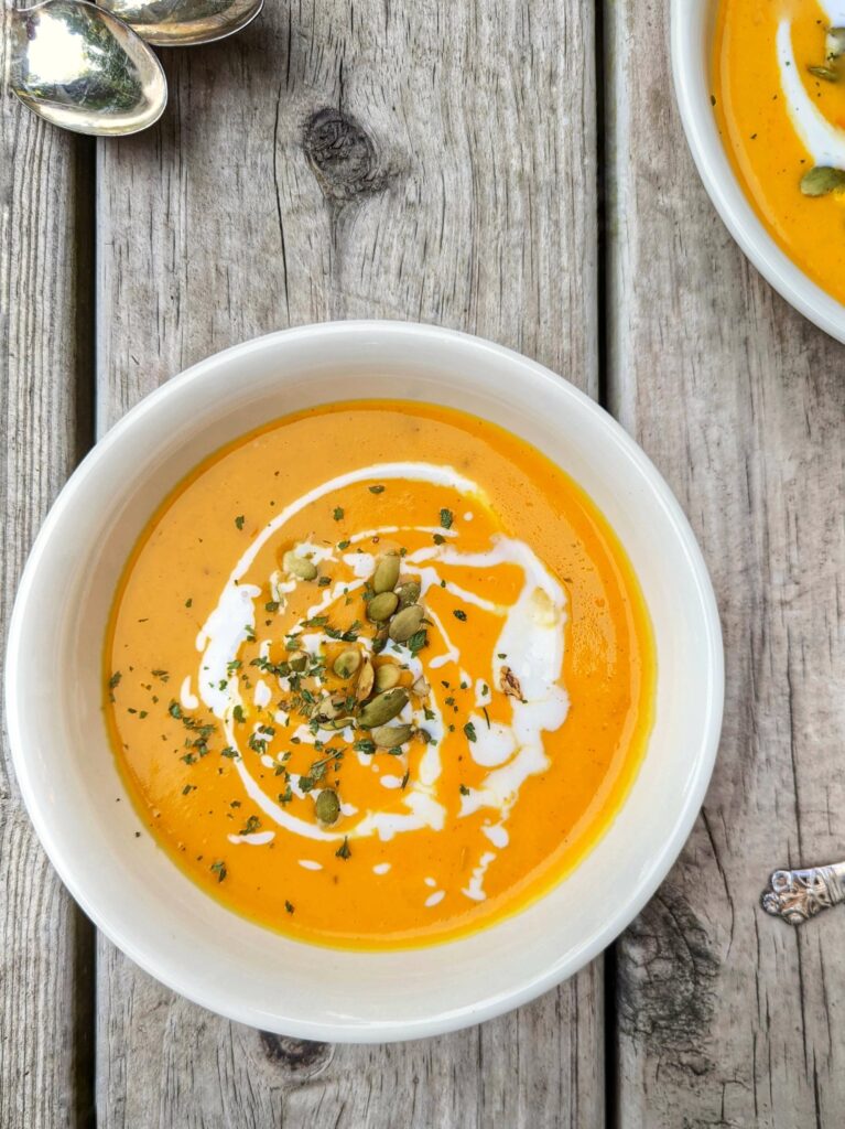A bowl of butternut soup garnished with a drizzle of coconut milk and toasted pepitas.