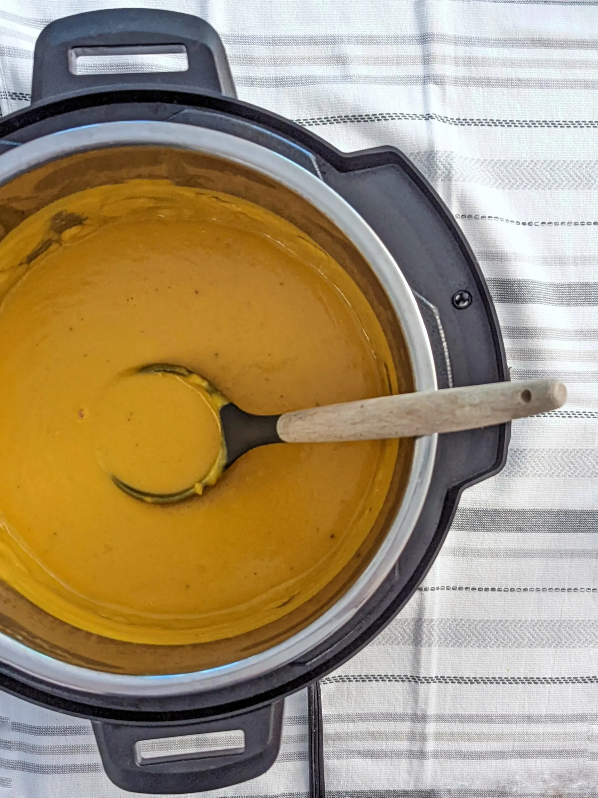 A spoonful of butternut squash soup held over the Instant Pot after stirring in the coconut milk.
