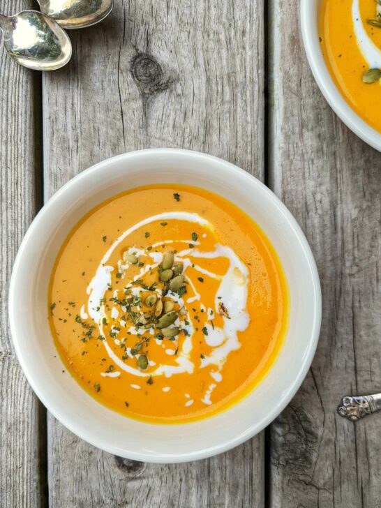 A bowl of butternut soup garnished with a drizzle of coconut milk and toasted pepitas.
