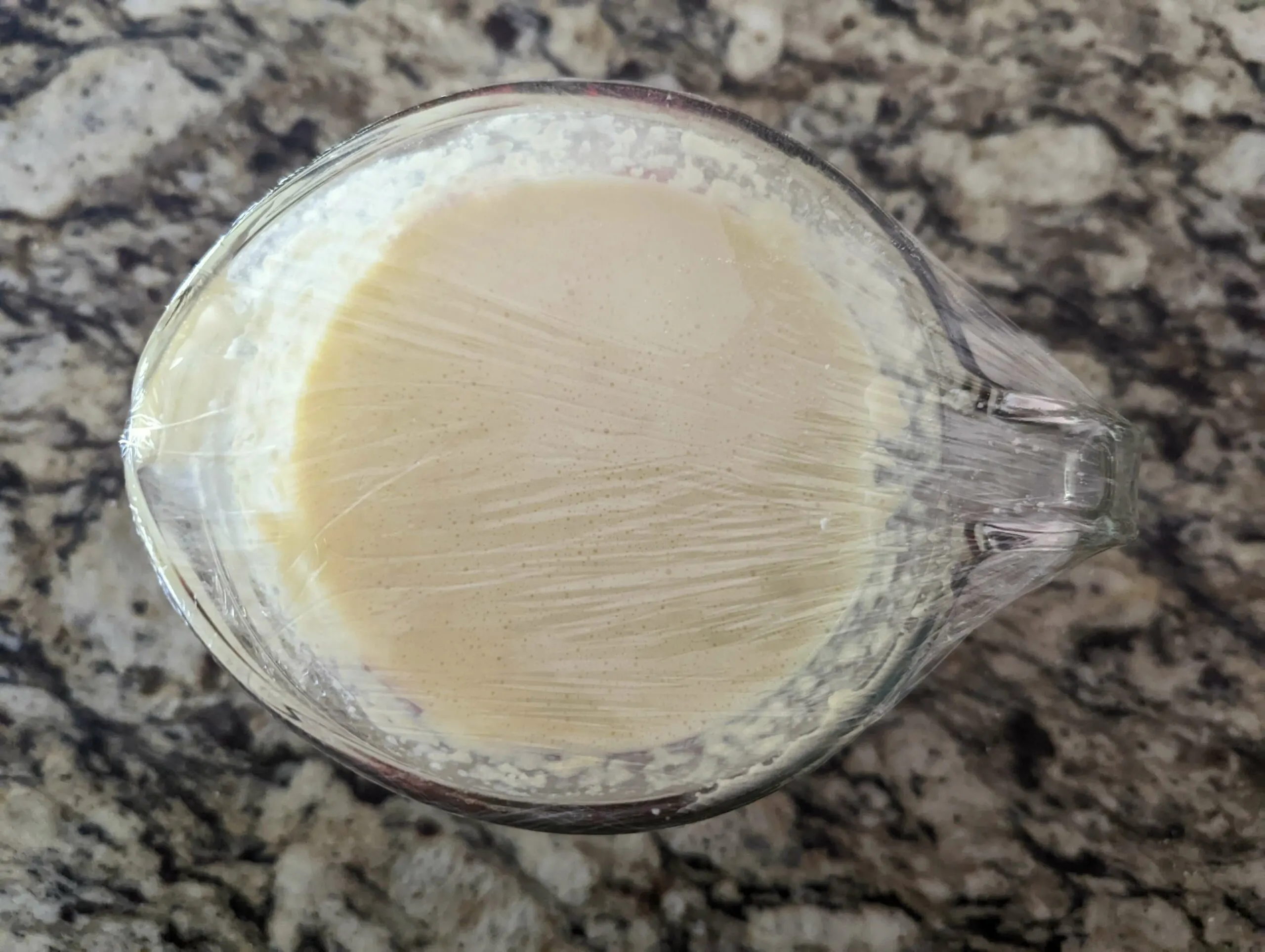The batter in a measuring cup covered with plastic wrap to rest. 