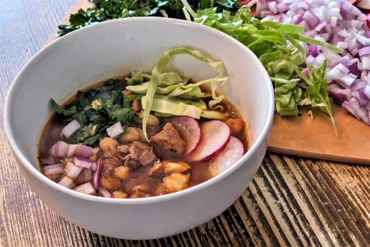 A single serving of Instant Pot pozole rojo garnished with fresh cilantro, onion, cabbage, and radish.