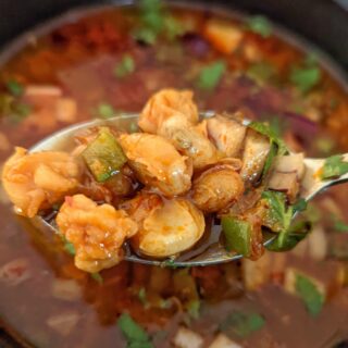 A single serving of pozole rojo garnished with fresh cilantro and red onion.