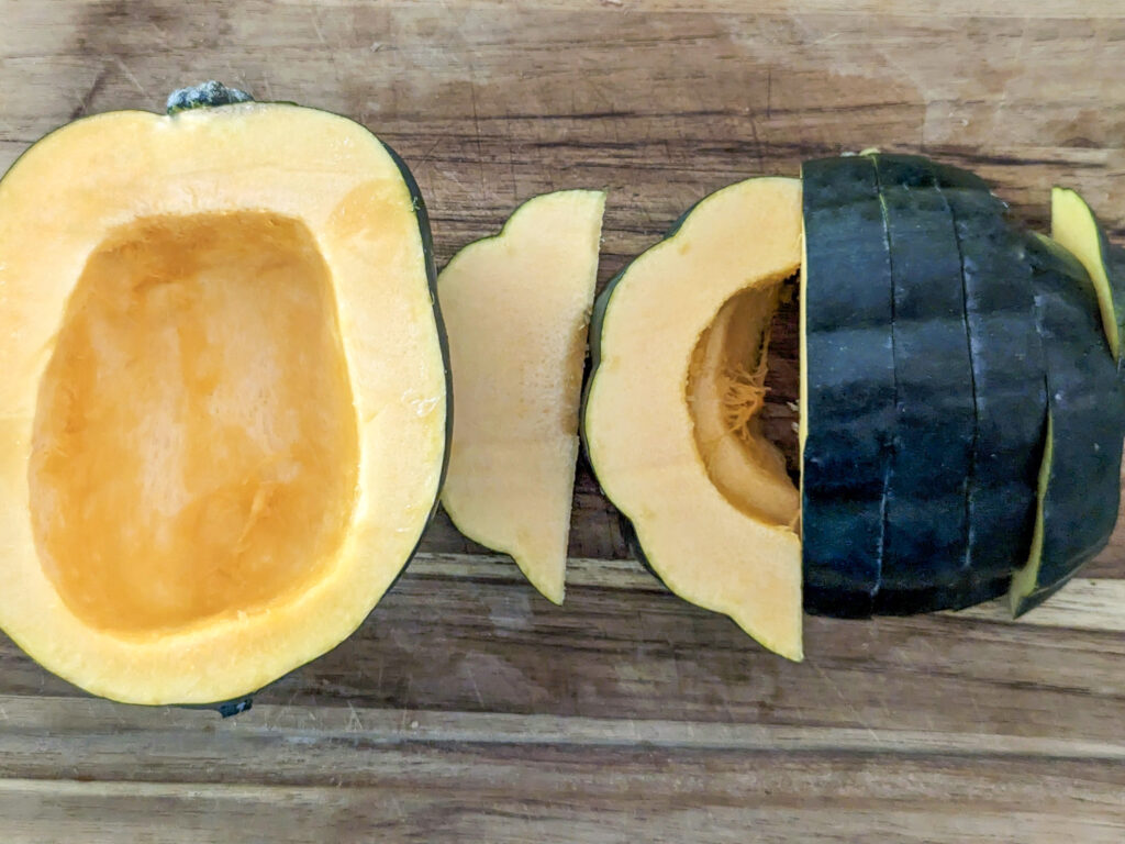 An acorn squash cut in half and cut into strips on a cutting board.