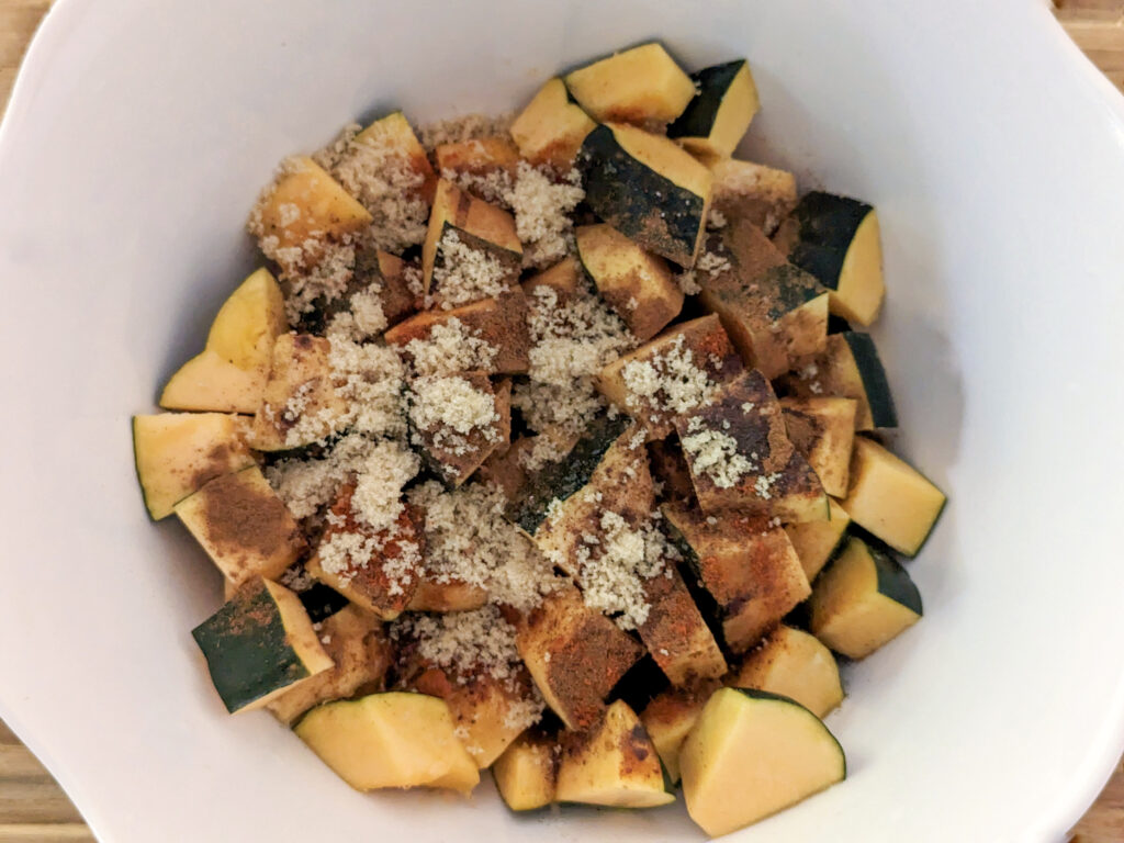 Acorn squash pieces tossed with sugar and spices in a mixing bowl.