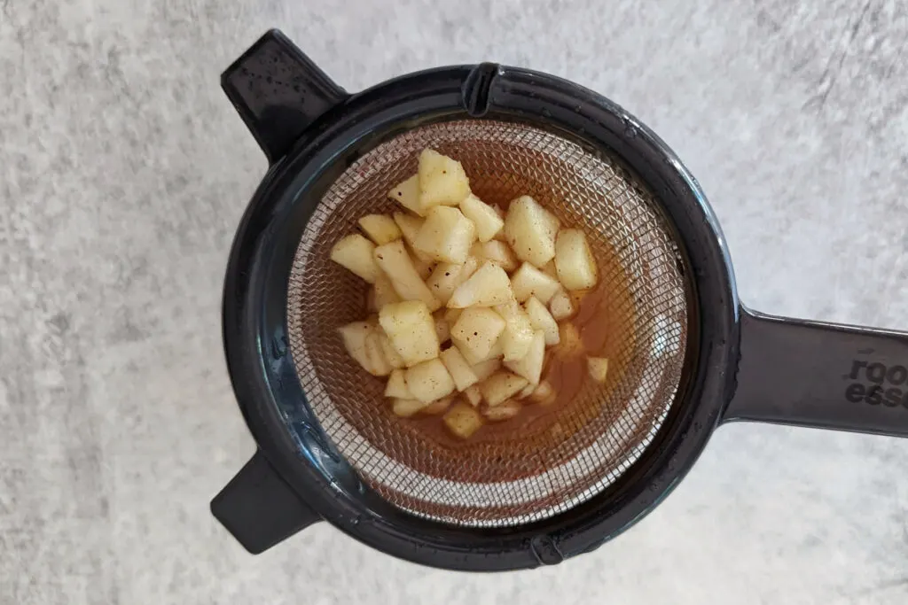 Straining the apples from the apple crisp simple syrup with a mesh sieve.
