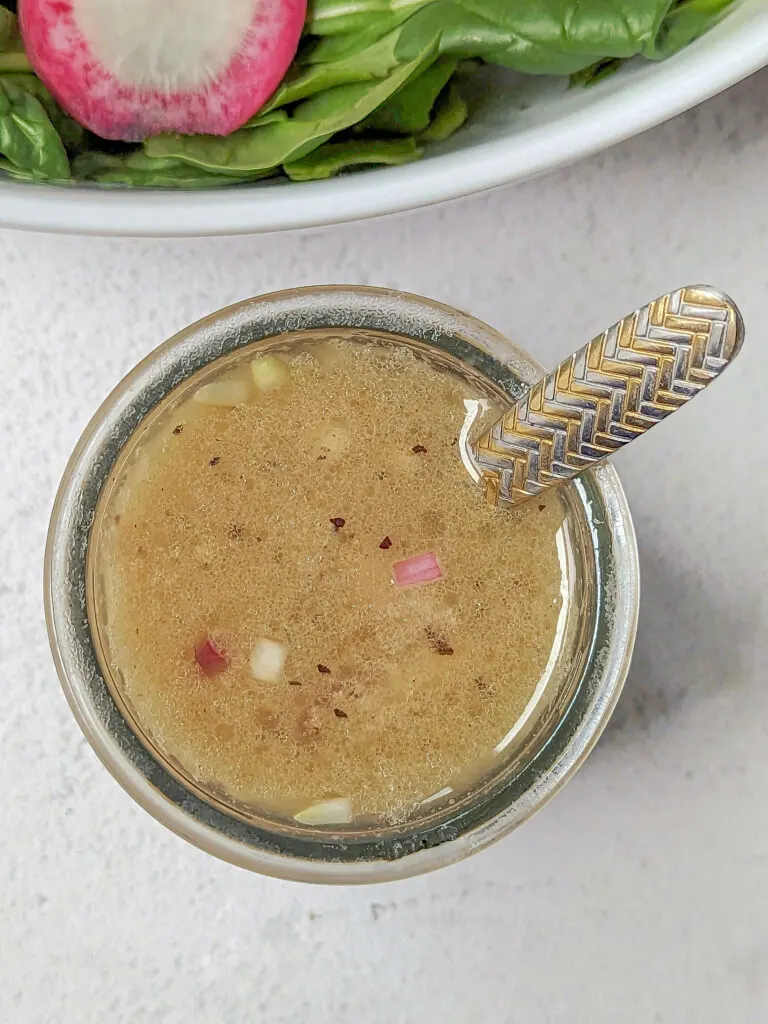 Sherry shallot dressing in a container in front of a salad.