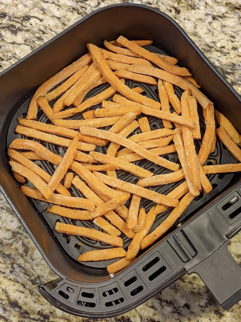 Frozen sweet potato fries in the air fryer basket.