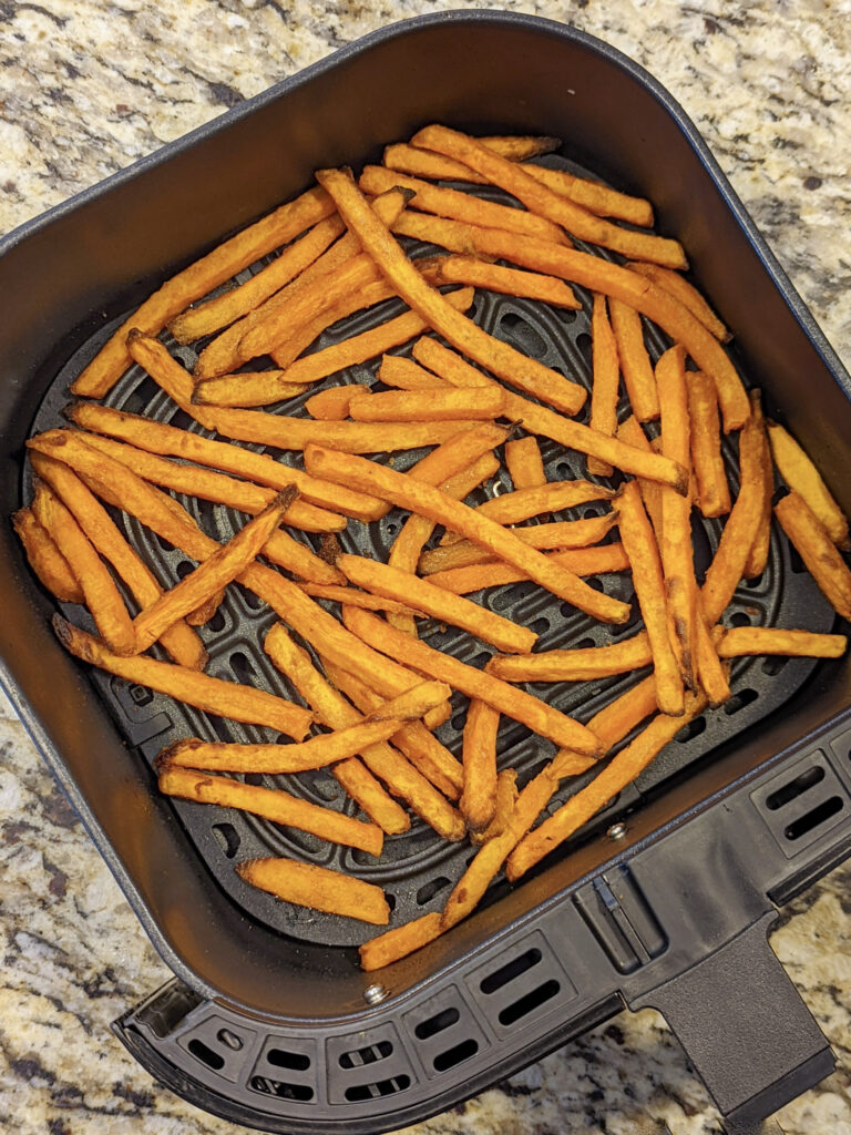 Frozen sweet potato fries in an air fryer basket fully cooked.