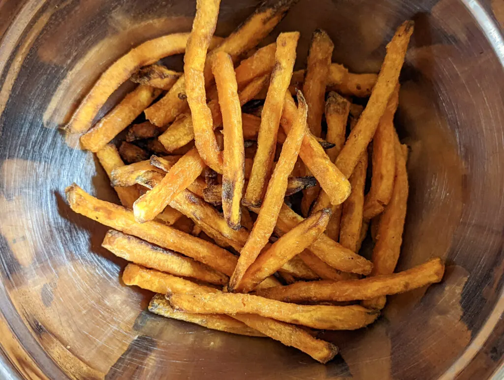 Tossing the sweet potato fries in a mixing bowl with spices.