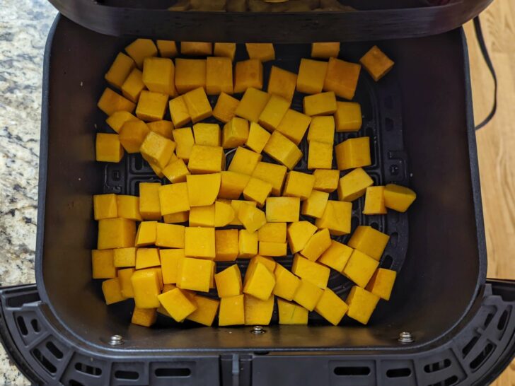 Cubes of butternut squash added to the air fryer basket.