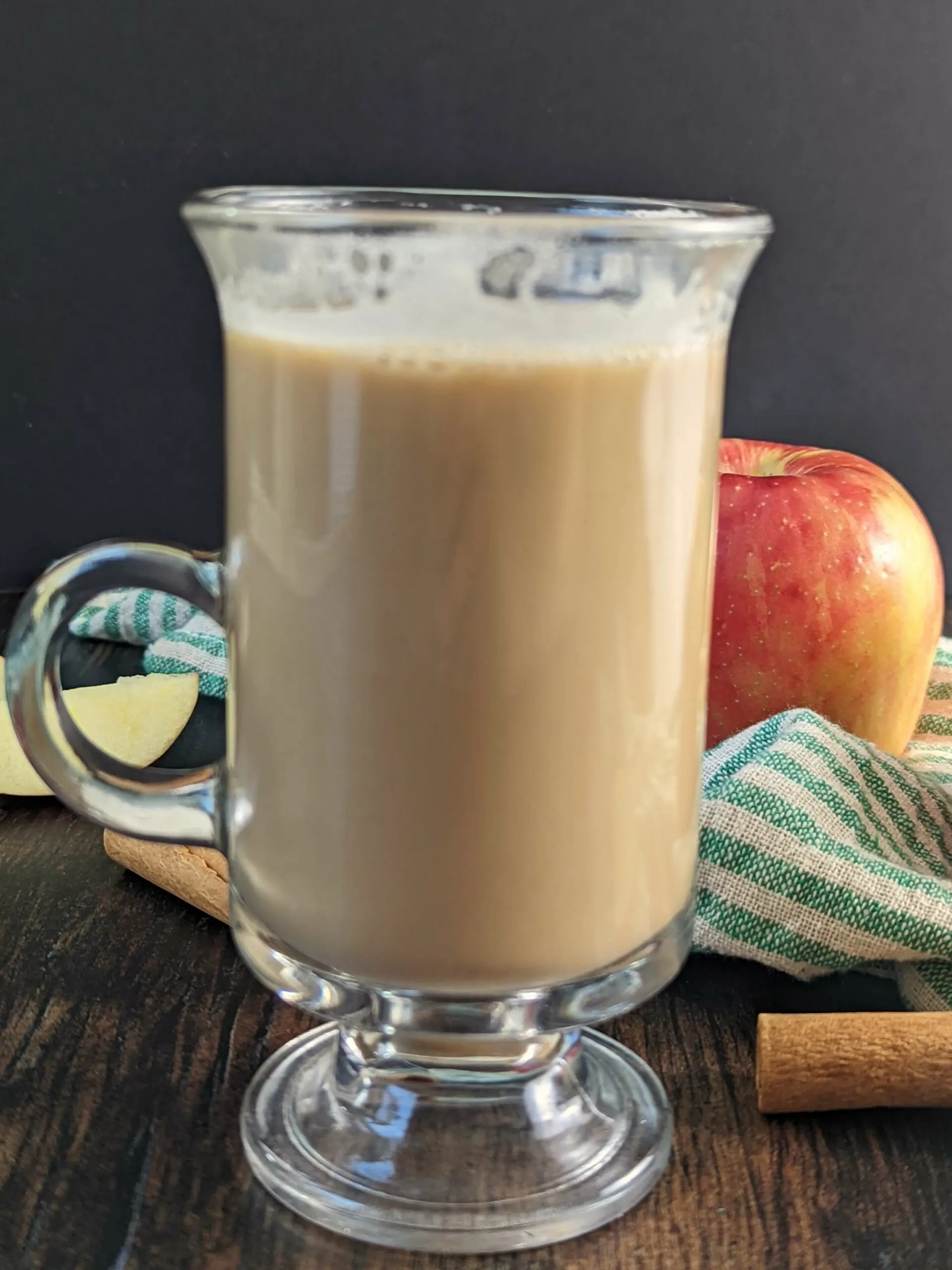 A glass of hot Apple Crisp Macchiato Recipe with apples in the background.