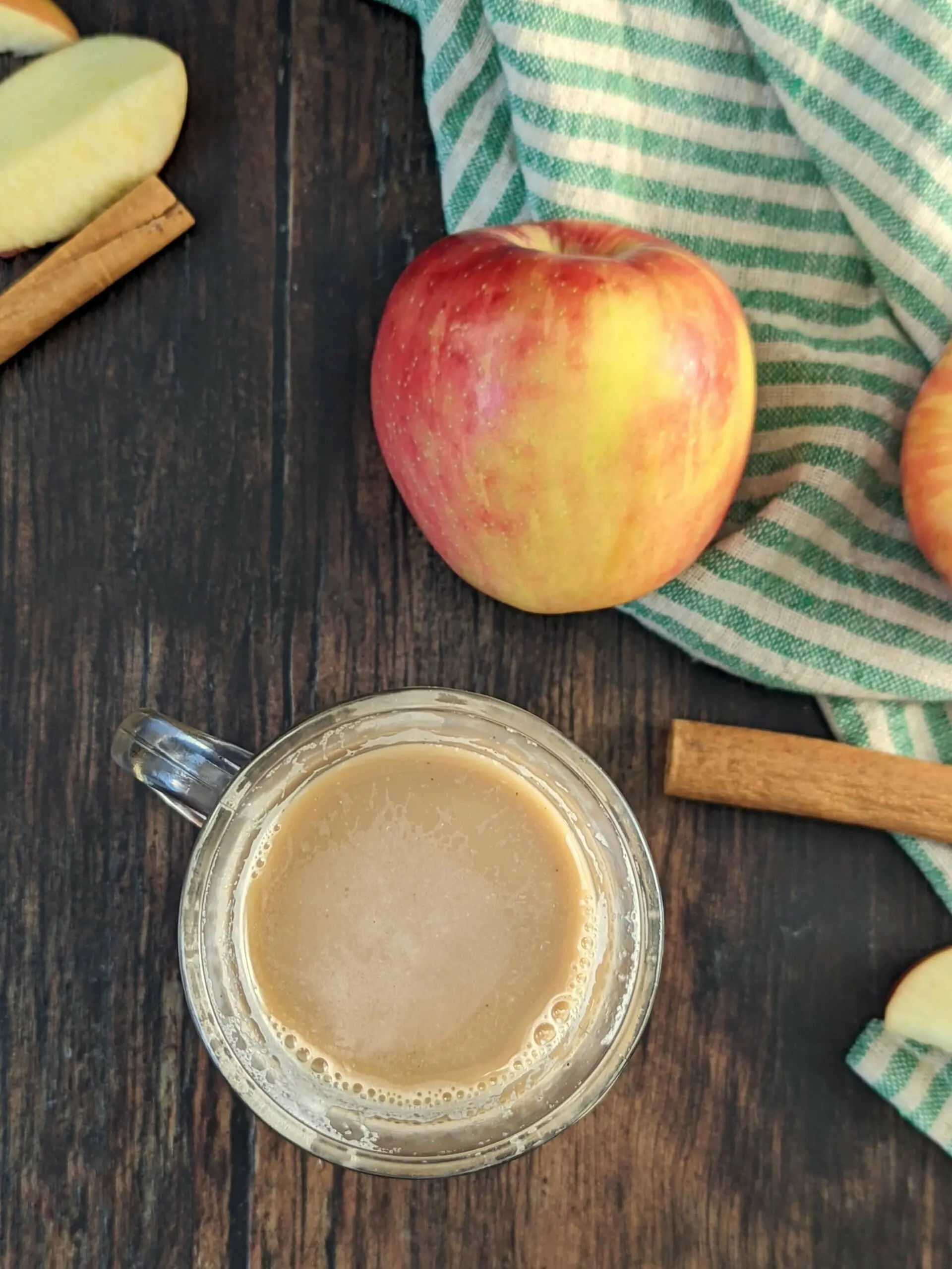 A glass of hot Apple Crisp Macchiato Recipe with apples in the background.