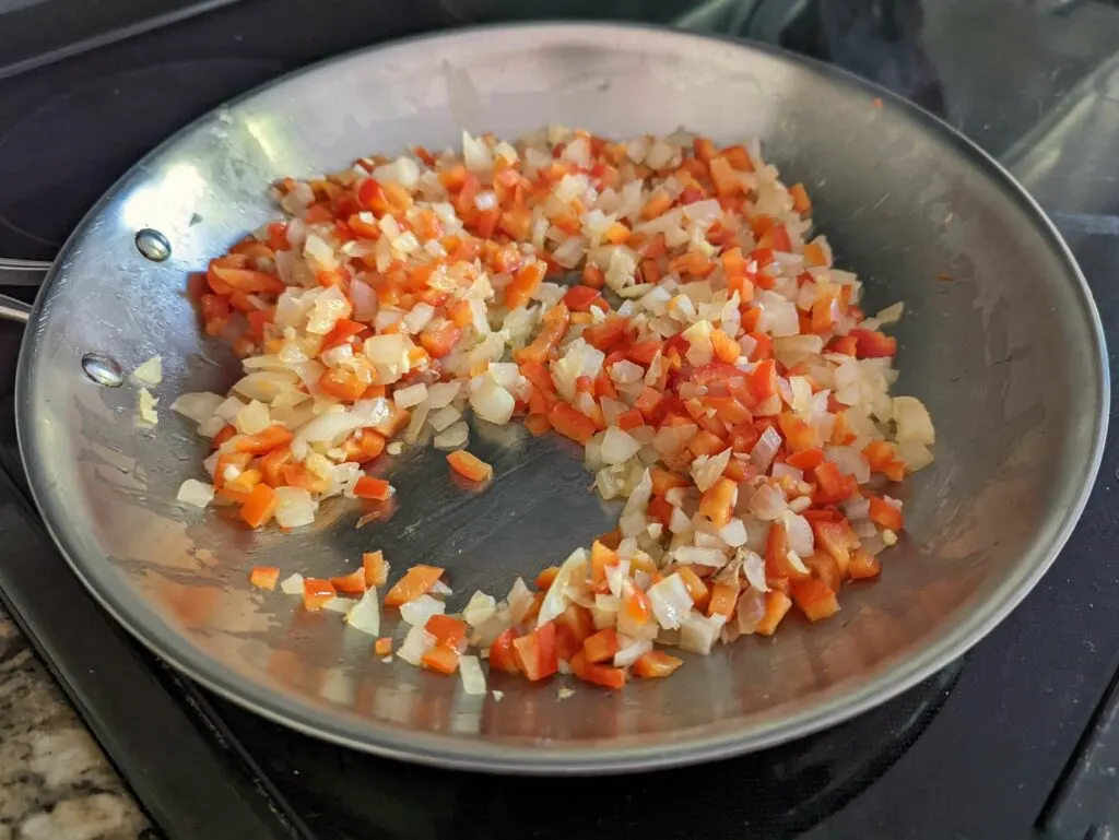 Onions, red bell pepper, and garlic cooking in a large skillet.