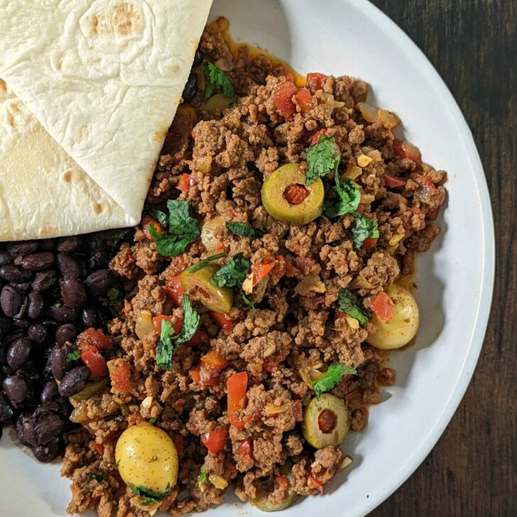 Beef picadillo on a plate black beans and a flour tortilla.