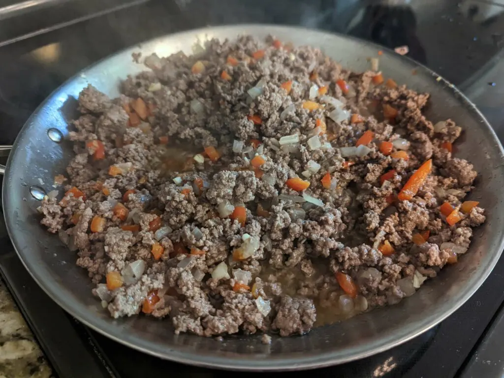 Ground beef cooking in a skillet with onions and peppers. 
