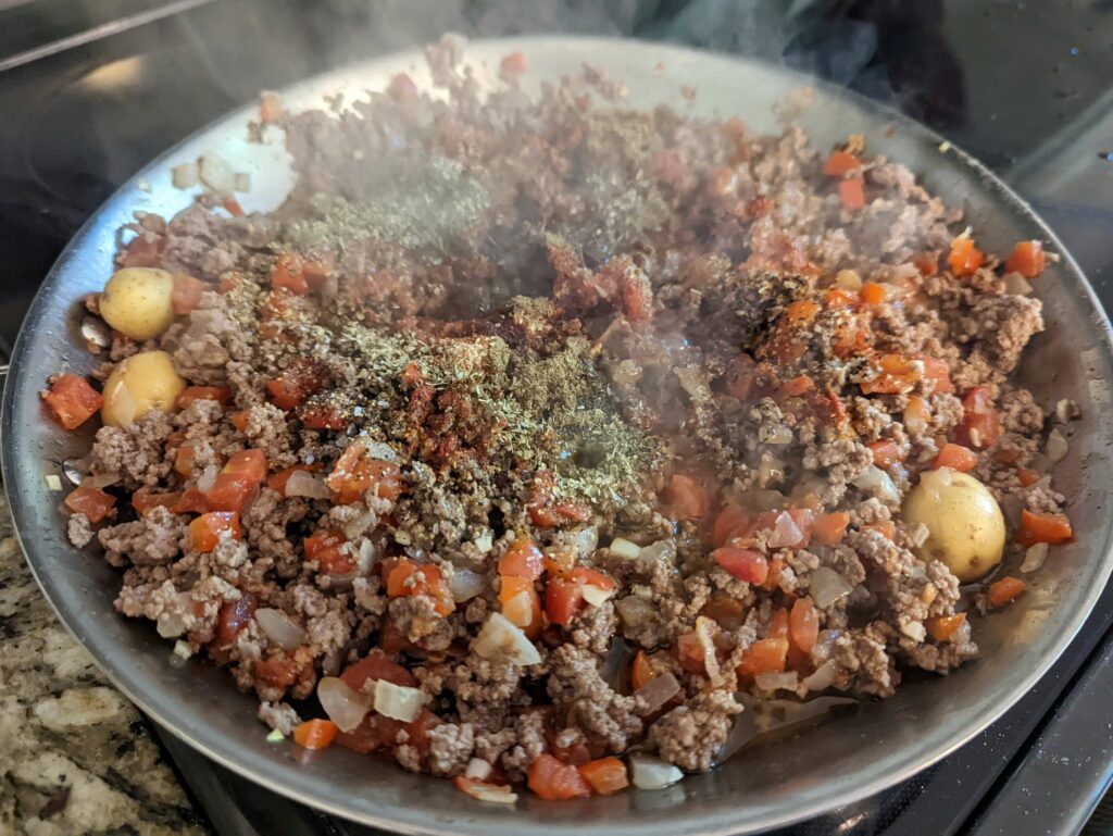 Beef picadillo simmering in a skillet with potatoes. 