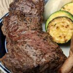 Bison steak on a plate with sweet potatoes and zucchini.