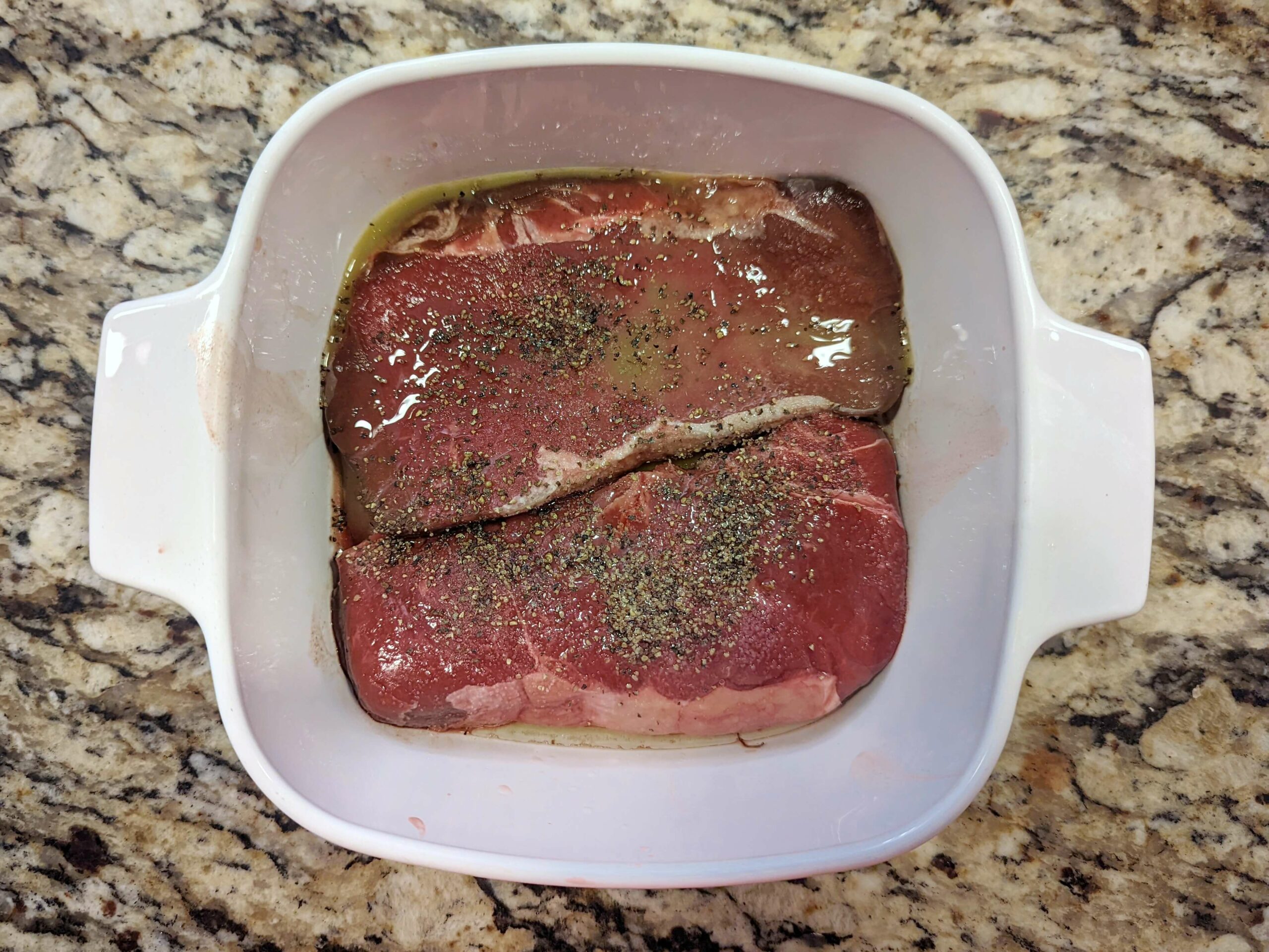 Bison steak in a dish with orange juice, salt, and pepper.